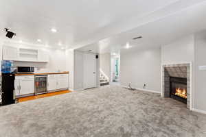 Unfurnished living room featuring beverage cooler, light carpet, bar, stairway, and recessed lighting