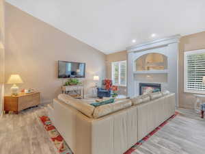 Living area featuring light wood-style floors, a glass covered fireplace, baseboards, lofted ceiling, and recessed lighting