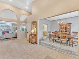 Dining area with a towering ceiling, recessed lighting, a warm lit fireplace, a chandelier, and baseboards