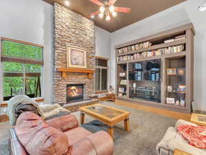 Living area featuring a stone fireplace, a ceiling fan, a high ceiling, wood finished floors, and built in shelves