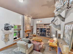 Living room featuring a stone fireplace, ceiling fan, and baseboards