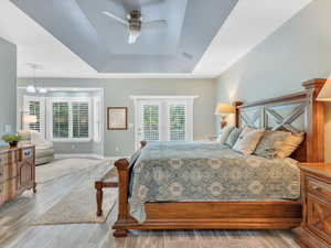 Bedroom featuring a tray ceiling, wood finished floors, access to outside, baseboards, and a chandelier