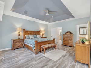 Bedroom with a tray ceiling, baseboards, light wood-type flooring, connected bathroom, and ceiling fan