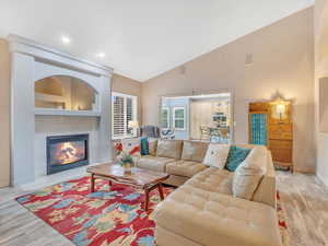 Living area featuring light wood-type flooring, baseboards, a tiled fireplace, high vaulted ceiling, and recessed lighting