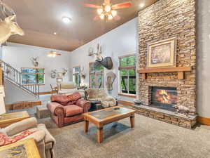 Living room featuring ceiling fan, carpet, a stone fireplace, baseboards, and stairway