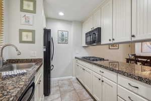 Kitchen featuring black appliances, a sink, baseboards, light tile patterned floors, and white cabinets