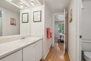 Bathroom featuring wood finished floors, toilet, vanity, baseboards, and connected bathroom
