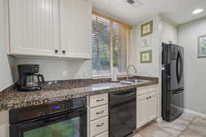 Kitchen with black appliances, a sink, dark countertops, light tile patterned floors, and white cabinets
