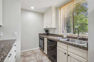 Kitchen featuring black appliances, a sink, dark countertops, light tile patterned floors, and baseboards