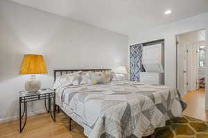 Bedroom with estacked washer and dryer, wood finished floors, a closet, recessed lighting, and baseboards