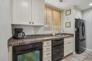 Kitchen featuring black appliances, dark countertops, a sink, light tile patterned floors, and white cabinetry