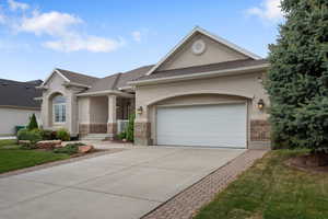 View of front of home with stucco siding, concrete driveway, an attached garage, and brick siding