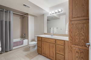 Bathroom with tile patterned floors, shower / bathtub combination with curtain, toilet, and vanity