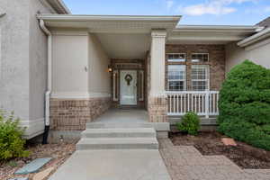 Entrance to property featuring brick siding, stucco siding, and covered porch