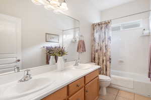 Bathroom featuring toilet, tile patterned flooring, double vanity, and shower / tub combo with curtain