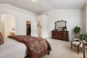 Bedroom featuring vaulted ceiling, light carpet, ensuite bathroom, a walk in closet, and baseboards
