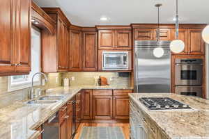 Kitchen with built in appliances, light stone countertops, a sink, hanging light fixtures, and brown cabinets