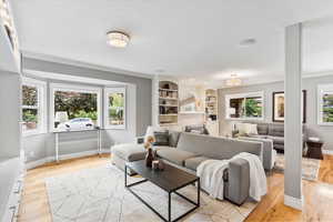 Living room featuring ornamental molding, light wood finished floors, a tiled fireplace, baseboards, and built in shelves