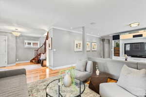 Living area with crown molding, light wood-type flooring, stairway, baseboards, and recessed lighting