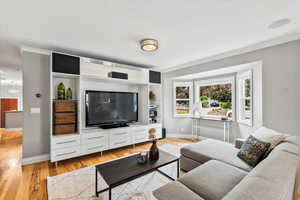 Living room with baseboards, light wood finished floors, and ornamental molding