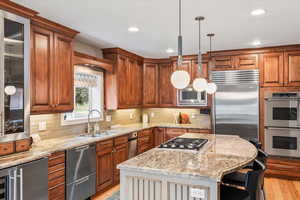 Kitchen featuring built in appliances, a sink, light stone counters, a kitchen bar, and recessed lighting