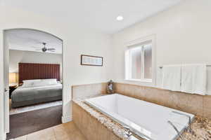 Ensuite bathroom with ceiling fan, tile patterned floors, and a garden tub