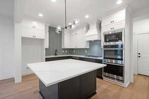 Kitchen featuring custom range hood, stainless steel appliances, a sink, white cabinets, and recessed lighting