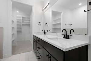 Bathroom with a walk in closet, double vanity, tile patterned flooring, and baseboards