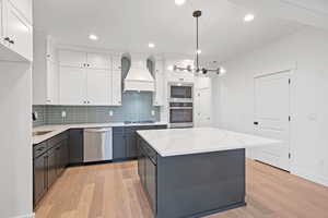 Kitchen featuring stainless steel appliances, custom exhaust hood, light wood-style floors, white cabinets, and recessed lighting