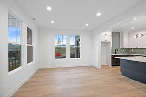 Kitchen with white cabinetry, light countertops, baseboards, decorative backsplash, and a sink
