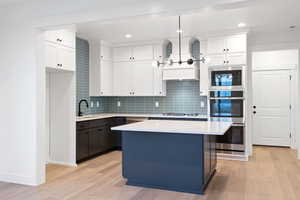 Kitchen with double oven, built in microwave, light wood-type flooring, white cabinets, and tasteful backsplash
