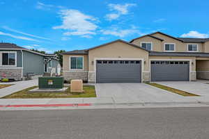 View of front of property with stone siding, stucco siding, concrete driveway, and a garage