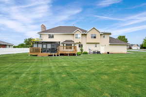 Back of property with a sunroom, a chimney, stucco siding, a wooden deck, and a shingled roof
