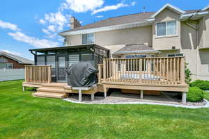 Rear view of house featuring stucco siding, a sunroom, a chimney, a deck, and roof with shingles