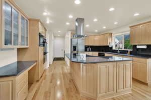Kitchen with black appliances, light brown cabinets, island range hood, a sink, and a center island