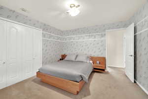 Carpeted bedroom featuring wallpapered walls and a closet