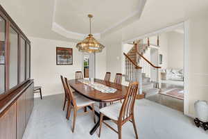 Dining area featuring light colored carpet, stairway, a tray ceiling, a chandelier, and crown molding