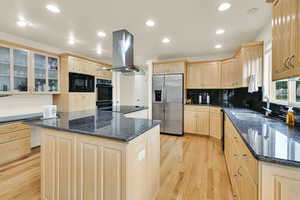 Kitchen with black appliances, island exhaust hood, a sink, light brown cabinetry, and light wood-style floors