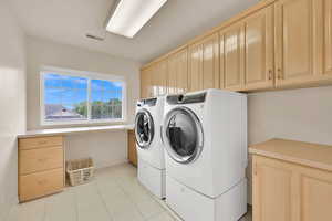 Clothes washing area featuring cabinet space, independent washer and dryer, baseboards, and light tile patterned floors