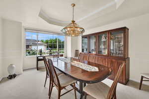 Dining room featuring a tray ceiling, a chandelier, baseboards, and light carpet