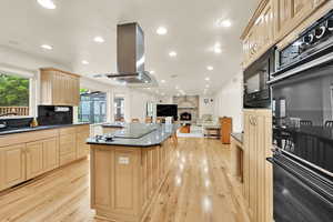 Kitchen with a sink, island exhaust hood, a kitchen island, black appliances, and light wood-style floors