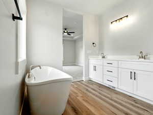 Full bathroom with wood finished floors, a freestanding bath, a ceiling fan, double vanity, and baseboards