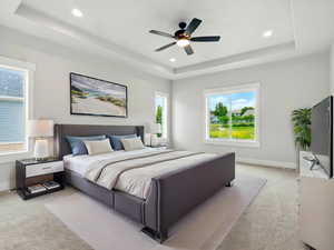 Bedroom with a raised ceiling, light carpet, multiple windows, and recessed lighting