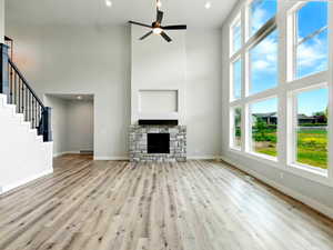 Unfurnished living room with a high ceiling, ceiling fan, wood finished floors, baseboards, and a stone fireplace