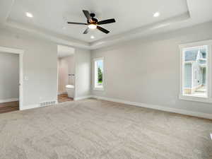 Unfurnished bedroom with a raised ceiling, light carpet, baseboards, recessed lighting, and ensuite bathroom