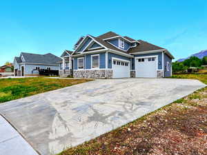Craftsman house with stone siding, a garage, concrete driveway, and a mountain view