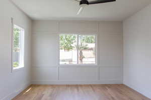 Empty room featuring a decorative wall, a ceiling fan, light wood-style flooring, and baseboards