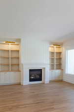 Unfurnished living room with a glass covered fireplace, light wood finished floors, built in features, and baseboards