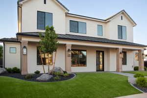 View of front of property featuring a standing seam roof, brick siding, a porch, a front lawn, and metal roof