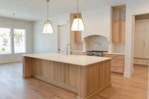 Kitchen with light wood finished floors, a sink, stove, and decorative backsplash